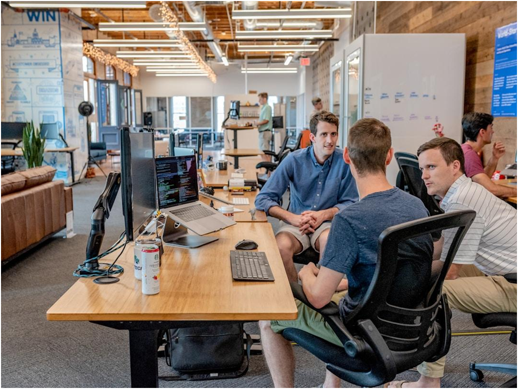Three men engaged in discussion at a table in an office, promoting collaboration and innovation in a knowledge-driven culture.